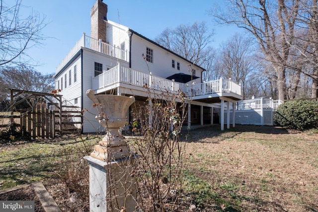 back of house featuring a deck, a lawn, and a chimney