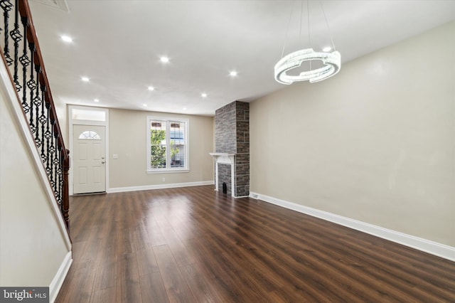 unfurnished living room with baseboards, dark wood-type flooring, stairs, a brick fireplace, and recessed lighting