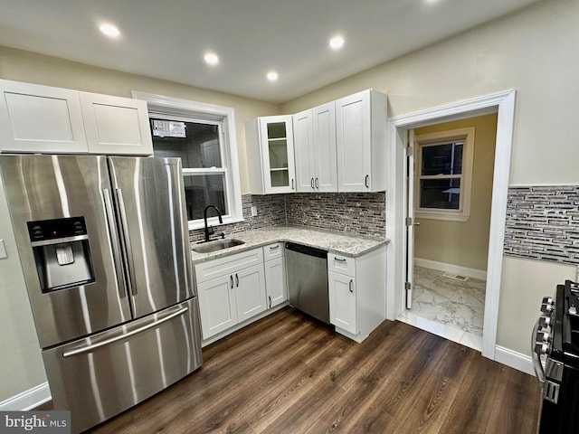 kitchen featuring light stone counters, a sink, white cabinets, appliances with stainless steel finishes, and glass insert cabinets