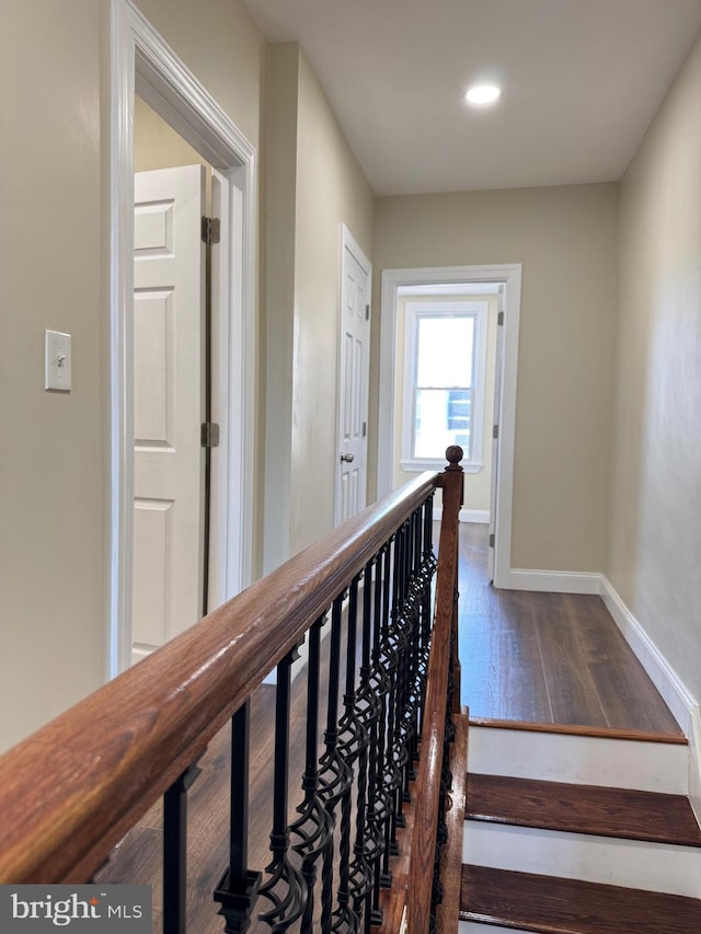 corridor with baseboards, dark wood-style flooring, and an upstairs landing