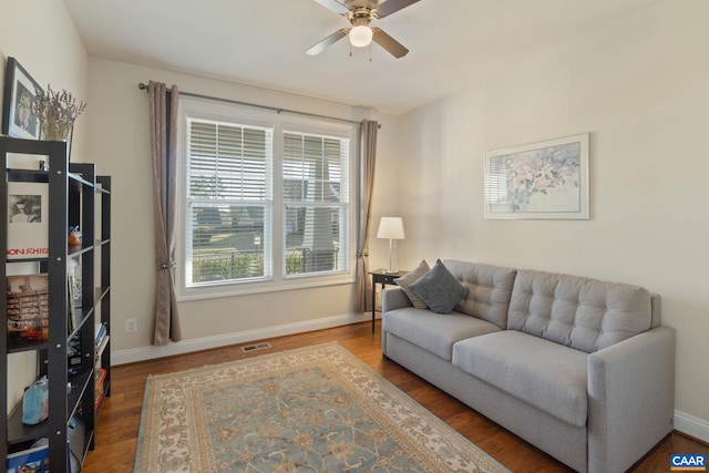 living room featuring a ceiling fan, visible vents, baseboards, and wood finished floors