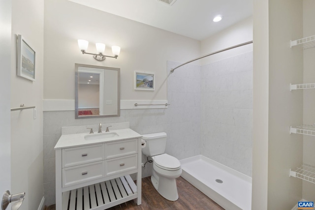 full bathroom featuring toilet, wood finished floors, a tile shower, vanity, and tile walls