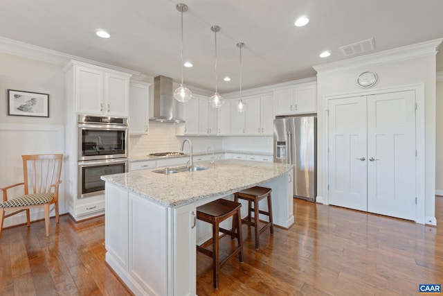 kitchen with stainless steel appliances, visible vents, white cabinets, a sink, and wall chimney exhaust hood