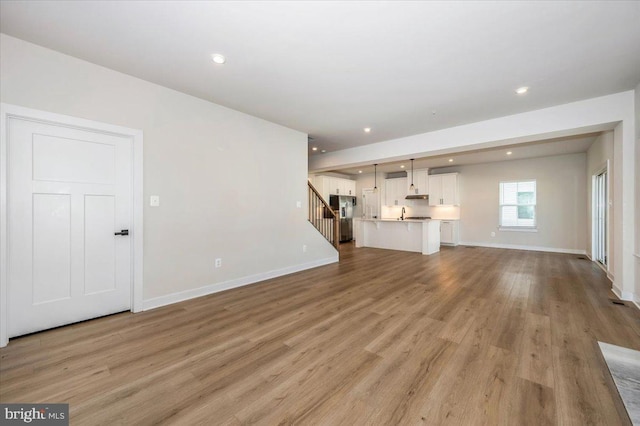 7508 Blue Sun Dr, Glen Burnie, MD 21060 - unfurnished living room featuring light wood finished floors, stairway, baseboards, and recessed lighting