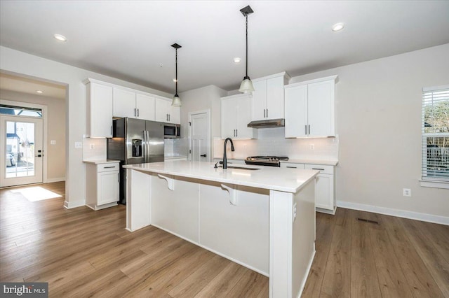 7508 Blue Sun Dr, Glen Burnie, MD 21060 - kitchen with under cabinet range hood, stainless steel appliances, wood finished floors, light countertops, and backsplash