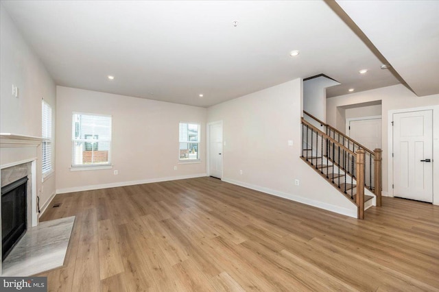 7508 Blue Sun Dr, Glen Burnie, MD 21060 - unfurnished living room with light wood-style floors, a healthy amount of sunlight, a premium fireplace, and stairs
