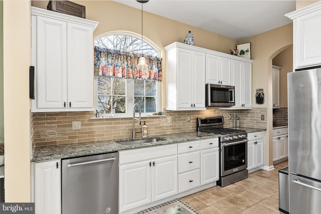 kitchen with decorative light fixtures, appliances with stainless steel finishes, white cabinetry, a sink, and dark stone countertops