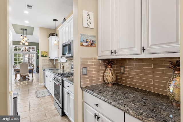 kitchen with stainless steel appliances, a sink, white cabinetry, dark stone counters, and pendant lighting