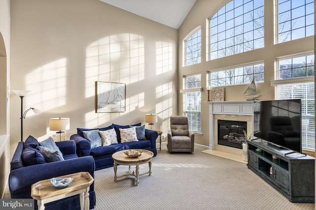 carpeted living area with baseboards, a premium fireplace, and high vaulted ceiling