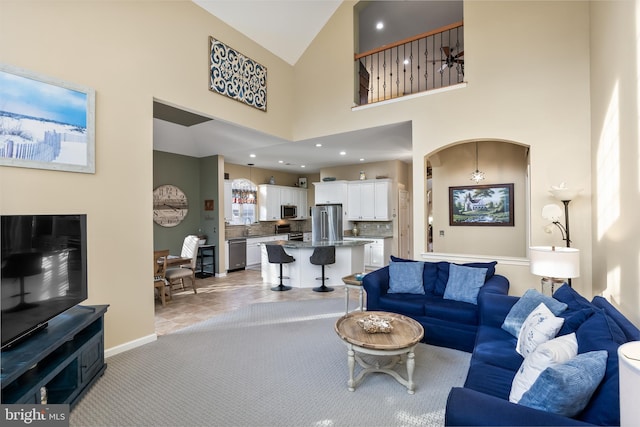 living area with recessed lighting, light colored carpet, a towering ceiling, and baseboards