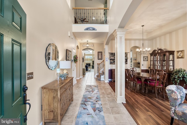 foyer featuring arched walkways, a towering ceiling, stairway, ornate columns, and a notable chandelier