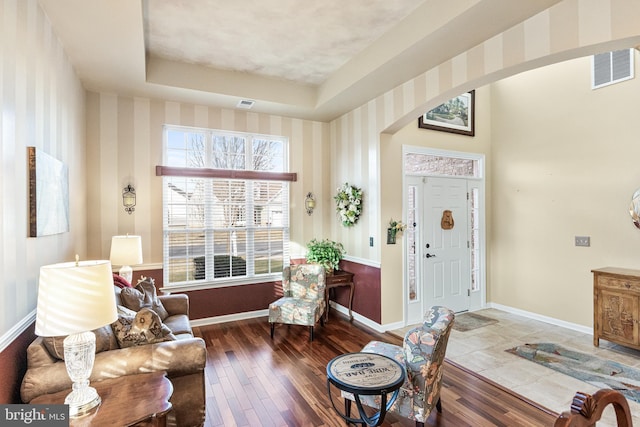 living area with arched walkways, dark wood-type flooring, visible vents, and baseboards