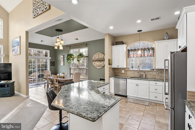 kitchen with visible vents, a kitchen island, appliances with stainless steel finishes, white cabinetry, and a sink