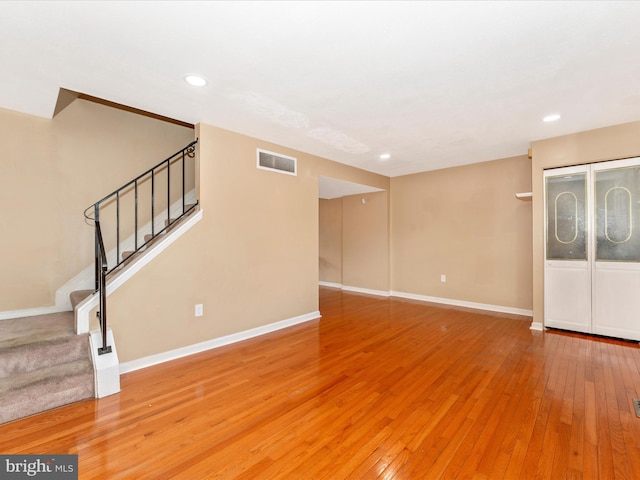 unfurnished living room with stairway, baseboards, visible vents, and hardwood / wood-style floors