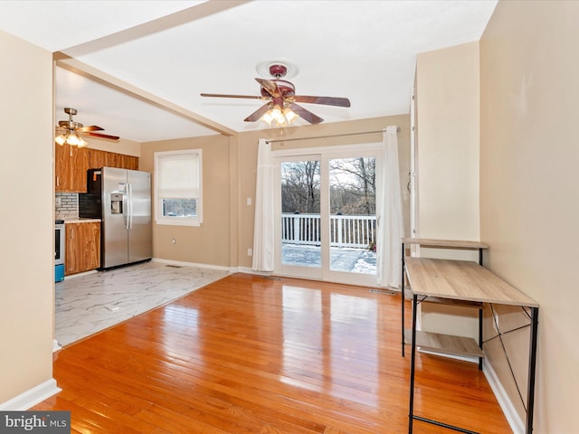 unfurnished living room featuring light wood-type flooring, a ceiling fan, and baseboards