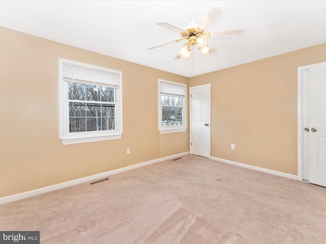 empty room featuring baseboards, visible vents, ceiling fan, and light colored carpet