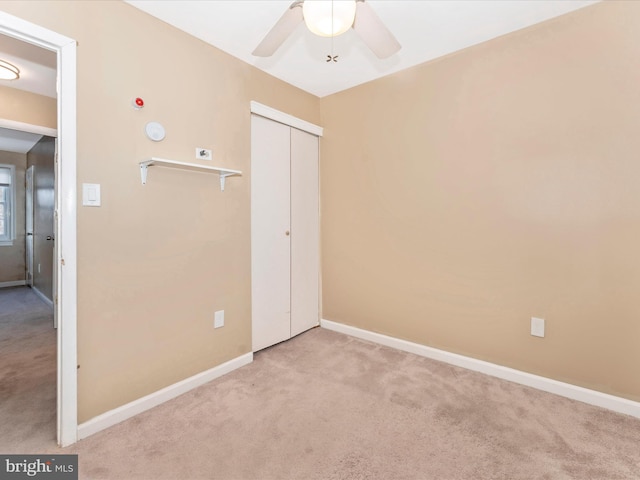 unfurnished bedroom with light carpet, ceiling fan, a closet, and baseboards