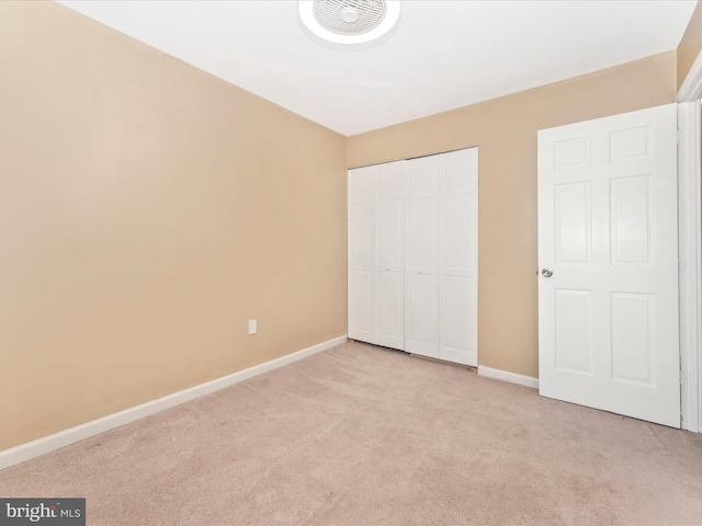 unfurnished bedroom featuring a closet, light colored carpet, and baseboards