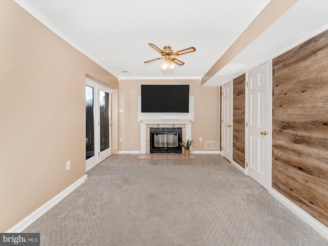 unfurnished living room with light colored carpet, visible vents, a tiled fireplace, wood walls, and baseboards