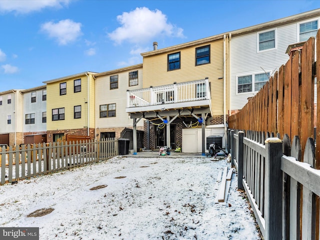 snow covered house with a fenced backyard, brick siding, and central AC unit