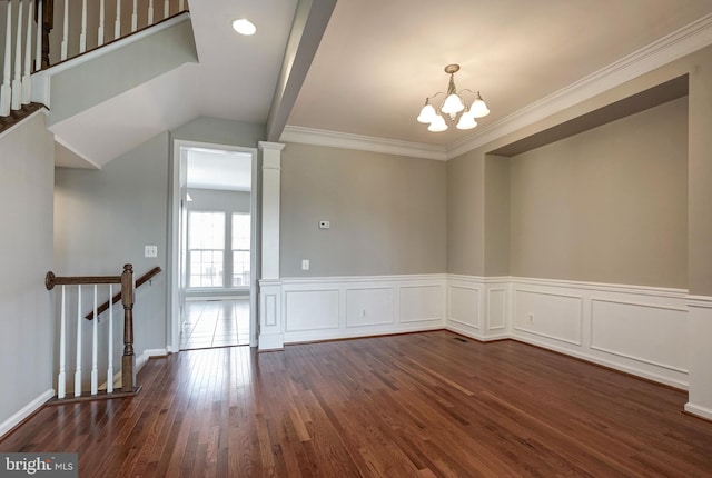 empty room featuring decorative columns, a wainscoted wall, ornamental molding, dark wood-style flooring, and a notable chandelier