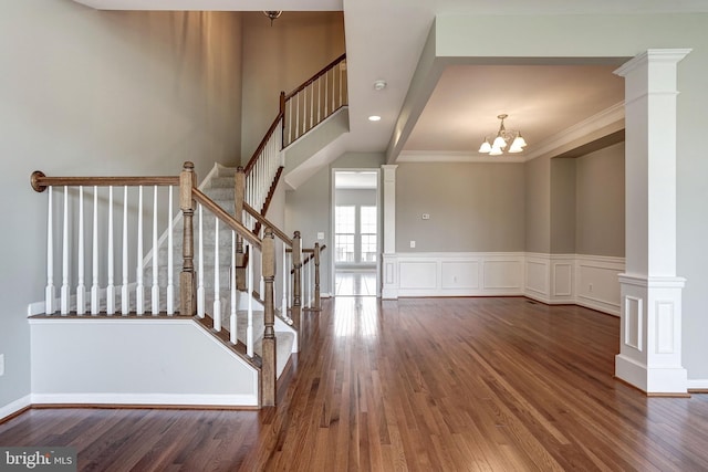 stairway featuring a decorative wall, a wainscoted wall, wood finished floors, decorative columns, and crown molding