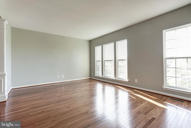 empty room with dark wood-style floors, baseboards, and visible vents