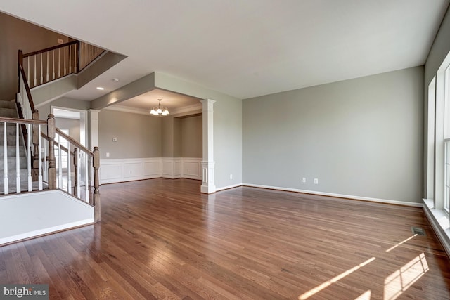 unfurnished living room featuring dark wood finished floors, wainscoting, stairway, ornate columns, and a chandelier