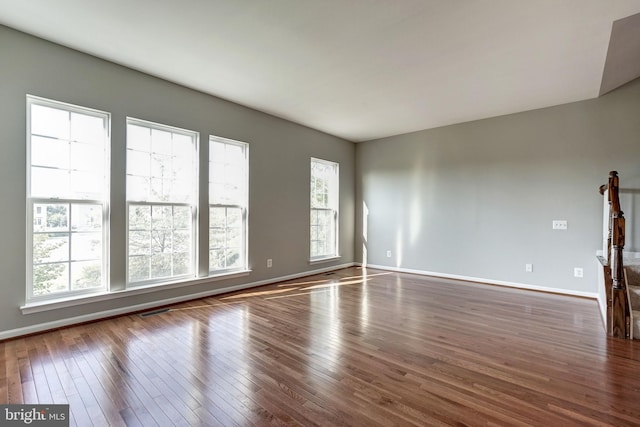 spare room with dark wood-type flooring, plenty of natural light, visible vents, and baseboards