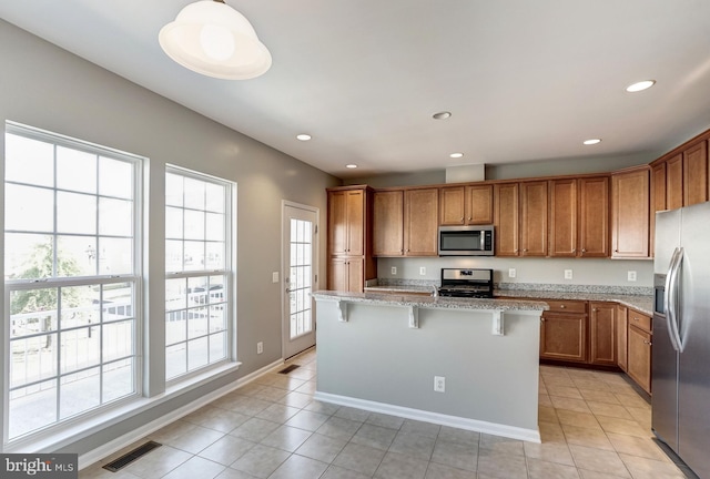 kitchen with a kitchen island, appliances with stainless steel finishes, a breakfast bar, brown cabinets, and light stone countertops