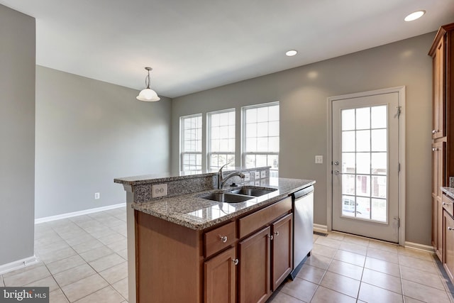 kitchen featuring pendant lighting, brown cabinetry, a kitchen island with sink, a sink, and dishwasher