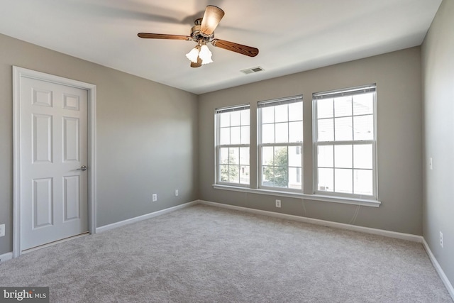 spare room with baseboards, visible vents, a ceiling fan, and light colored carpet