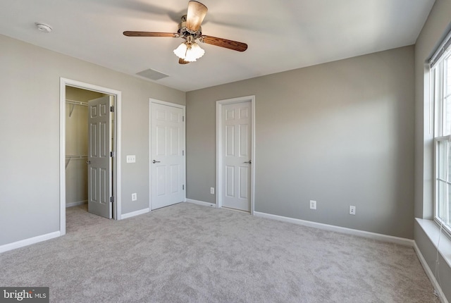 unfurnished bedroom featuring light carpet, a walk in closet, visible vents, and baseboards