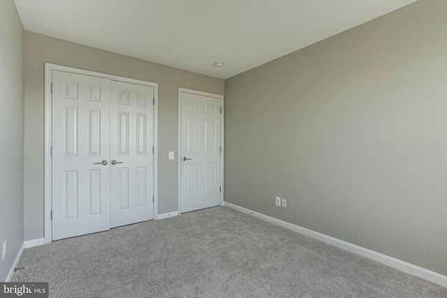 unfurnished bedroom with a closet, light carpet, and baseboards