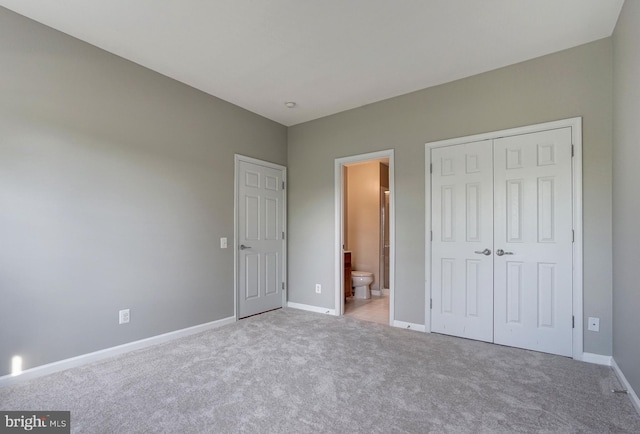 unfurnished bedroom with a closet, light colored carpet, baseboards, and ensuite bathroom