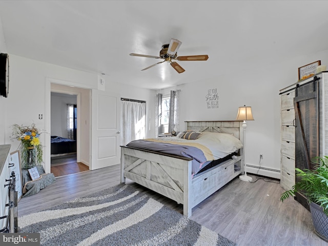 bedroom featuring a baseboard heating unit, a ceiling fan, wood finished floors, and a barn door