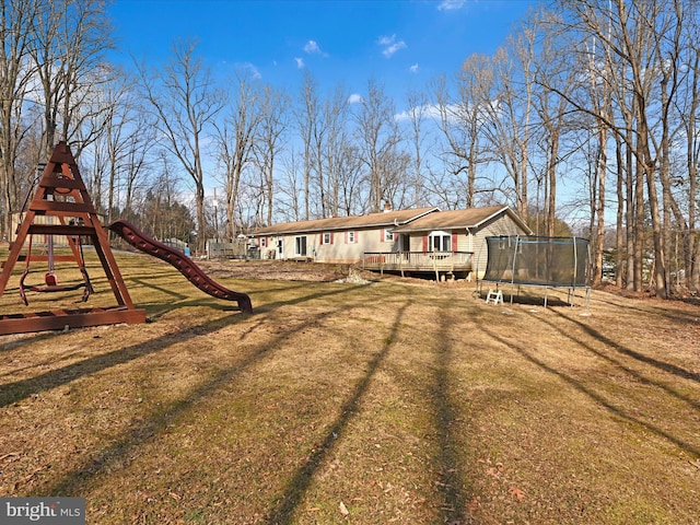 rear view of property with a trampoline, playground community, a yard, and a wooden deck