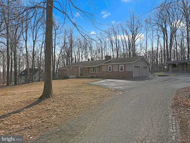 ranch-style home featuring an attached garage, driveway, a chimney, and brick siding