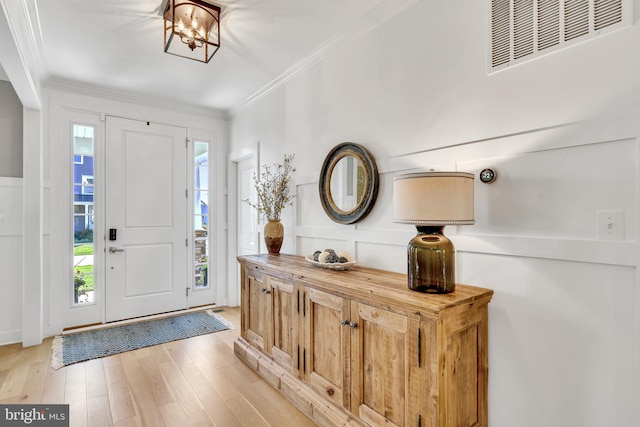 foyer entrance featuring light wood finished floors, ornamental molding, wainscoting, and visible vents