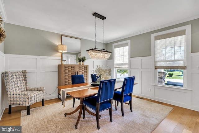 dining space with light wood-style floors, a decorative wall, and crown molding