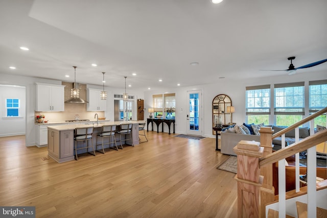 kitchen with white cabinets, a spacious island, wall chimney exhaust hood, open floor plan, and decorative light fixtures