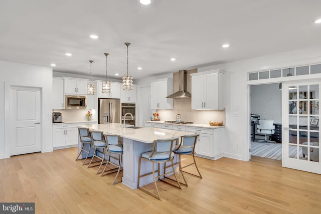 kitchen with appliances with stainless steel finishes, light countertops, wall chimney range hood, white cabinetry, and a sink