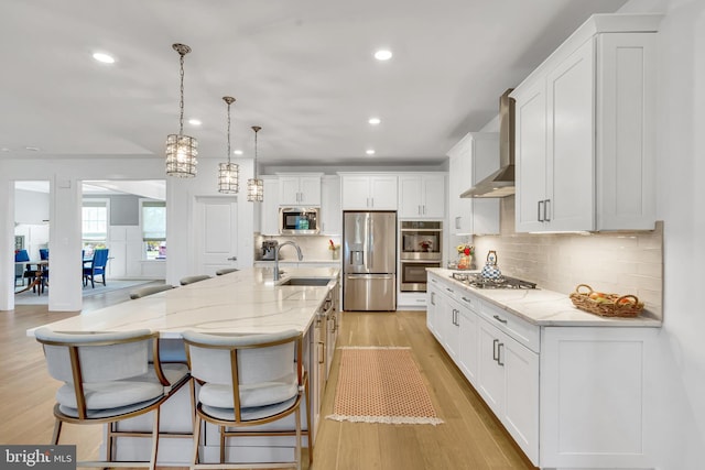 kitchen with appliances with stainless steel finishes, white cabinetry, a large island, and wall chimney range hood