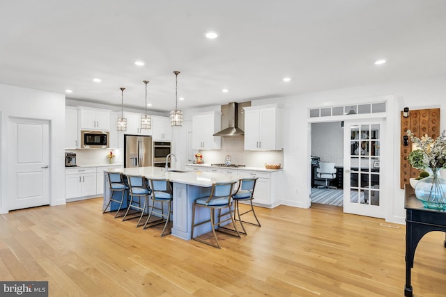 kitchen with stainless steel appliances, light countertops, wall chimney range hood, and white cabinetry