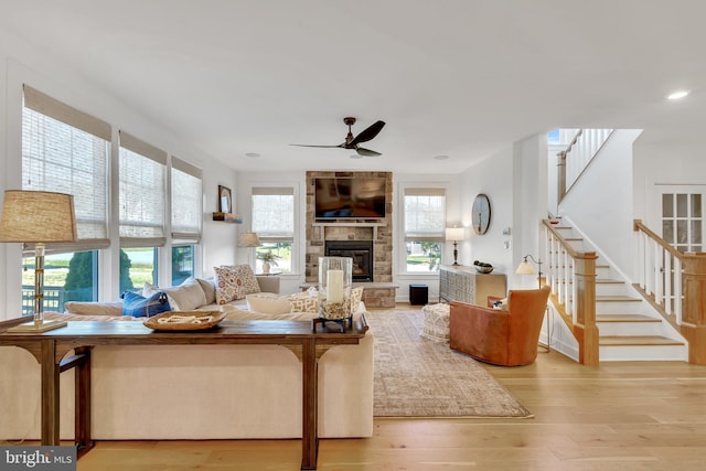 living area featuring a stone fireplace, light wood-style flooring, recessed lighting, a ceiling fan, and stairway