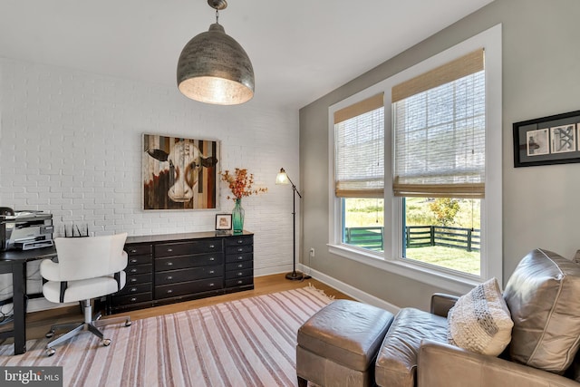 home office featuring light wood-type flooring, baseboards, and brick wall