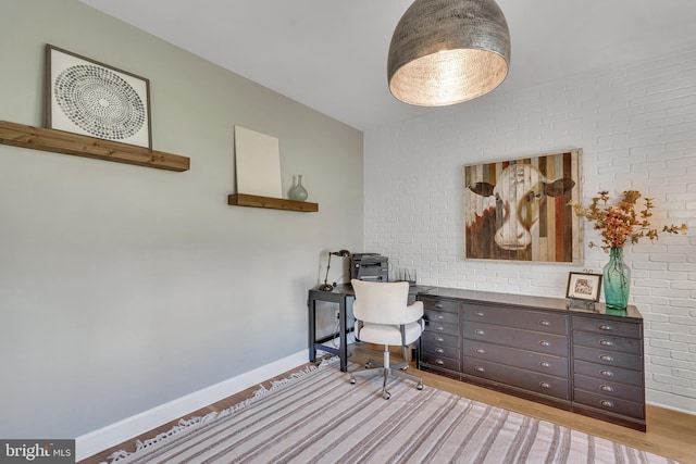 office with brick wall, light wood finished floors, and baseboards