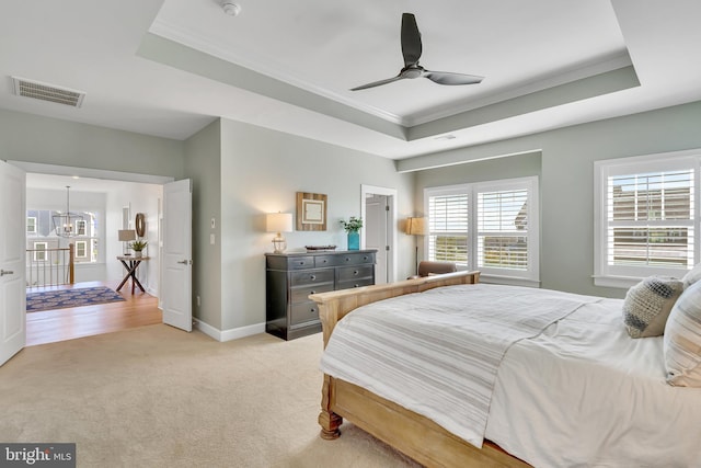 bedroom with light colored carpet, a tray ceiling, visible vents, and baseboards