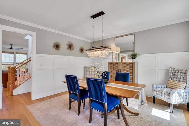 dining space with wainscoting, ornamental molding, stairs, light wood-style floors, and a decorative wall