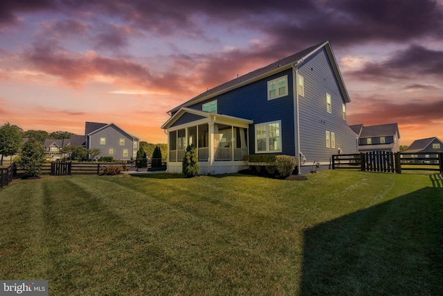 back of house at dusk featuring a yard, a fenced backyard, and a sunroom